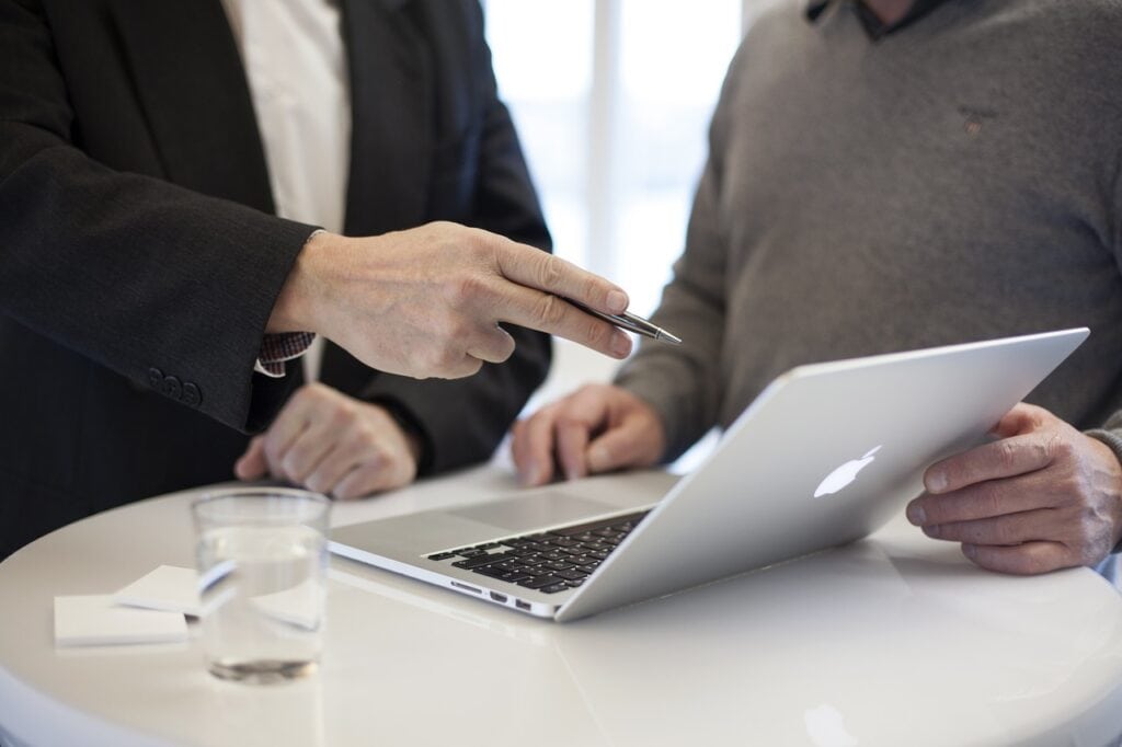 Cena de duas pessoas em reunião de negócios com um laptop, discutindo estratégias de trabalho e mostrando informações importantes com uma caneta.