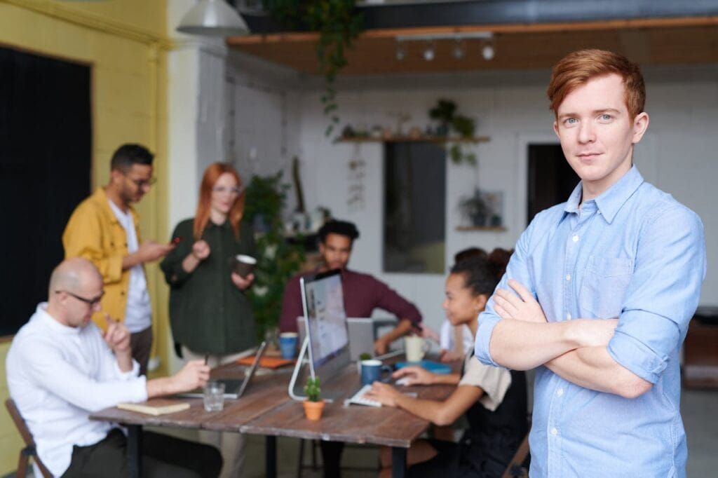 Grupo de profissionais em um ambiente de trabalho colaborativo, com foco em um jovem de camisa azul, simbolizando trabalho em equipe e inovação.