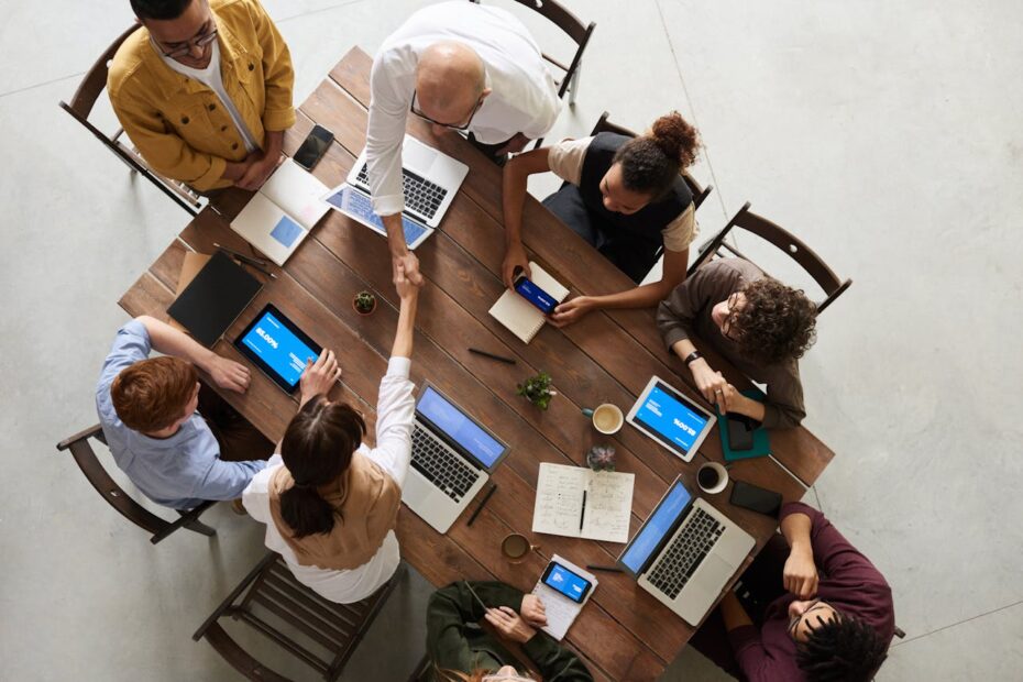 Reunião produtiva em equipe, com pessoas collaborando em laptops e tablets, realizando negócios e interagindo em um ambiente moderno.